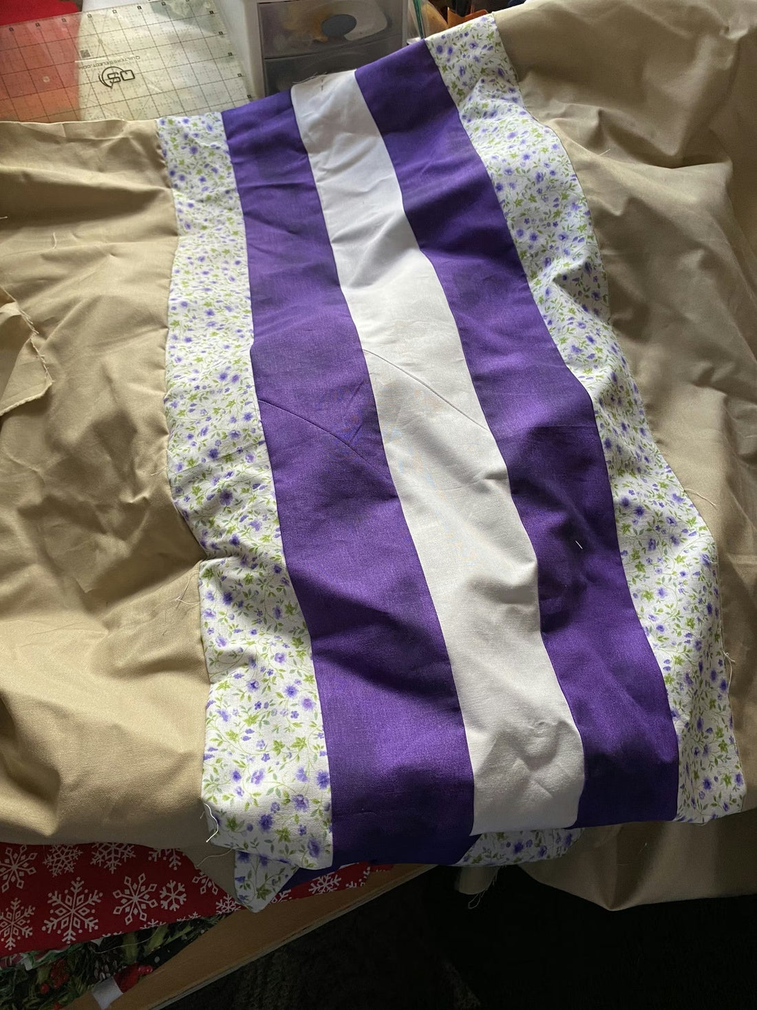 Quilted fabric backing being pieced with a wide center strip and coordinating side panels laid out on a cutting table