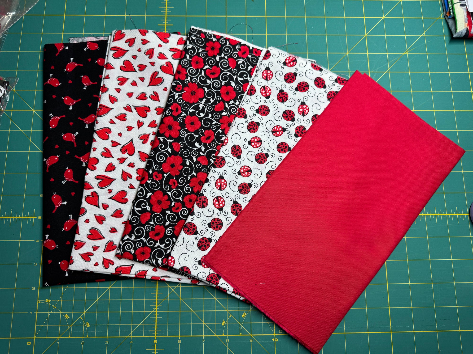 A selection of cotton fabric pieces in red, black, and white with various patterns including ladybugs, dots, and hearts on a quilting board.