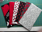 A selection of cotton fabric pieces in red, black, and white with various patterns including ladybugs, dots, and hearts on a quilting board.