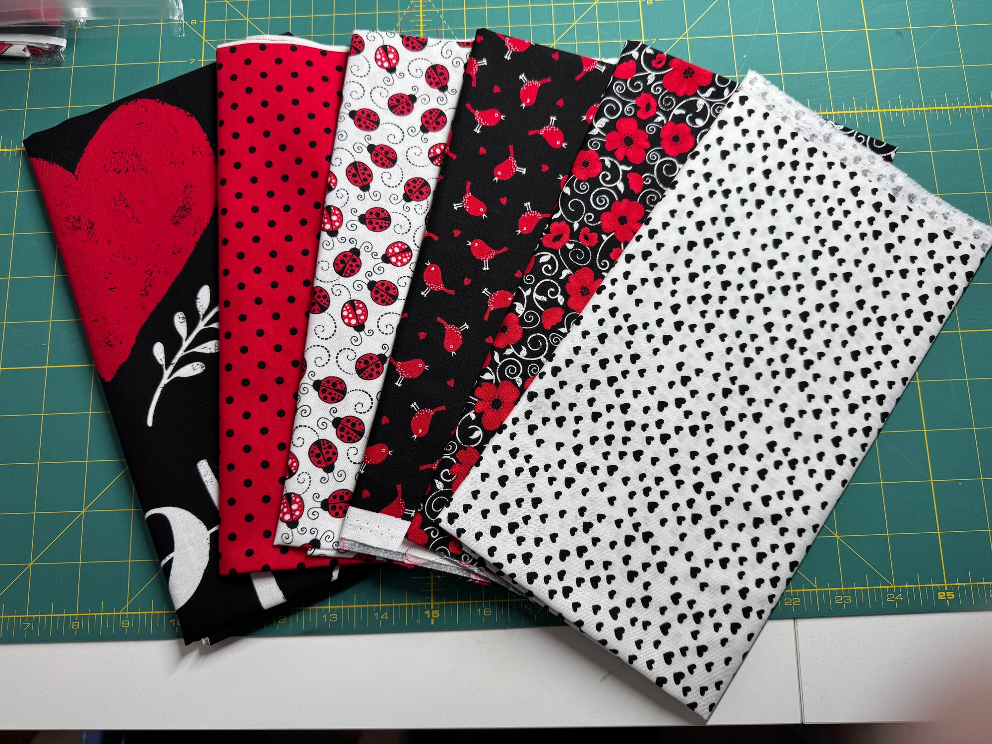 A selection of cotton fabric pieces in red, black, and white with various patterns including ladybugs, dots, and hearts on a quilting board.