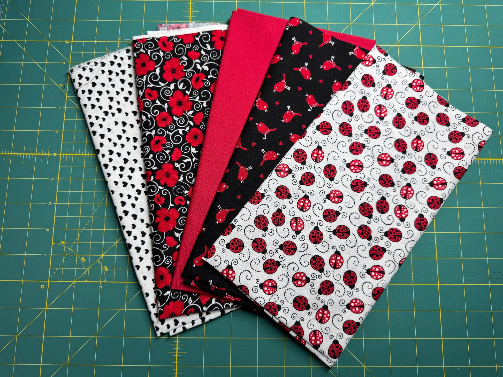 A selection of cotton fabric pieces in red, black, and white with various patterns including ladybugs, dots, and hearts on a quilting board.